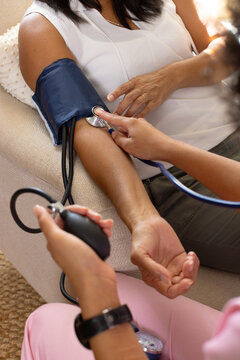 Mature biracial woman getting blood pressure checked by young biracial woman at home