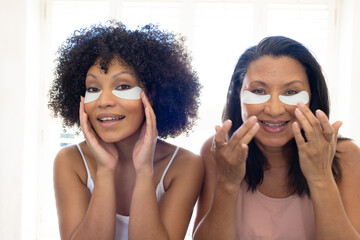 Biracial mother and daughter are applying skincare patches at home in the bathroom