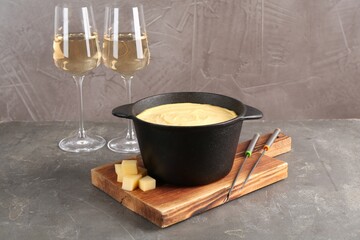 Fondue pot with tasty melted cheese, forks and wine on grey table