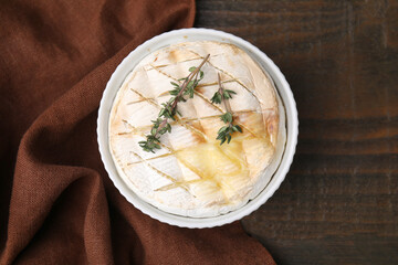 Tasty baked camembert and thyme in bowl on wooden table, top view