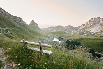 Wooden bench overlooking a majestic mountain vista invites peaceful contemplation. The setting sun casts a warm glow over the rugged landscape, promising adventure