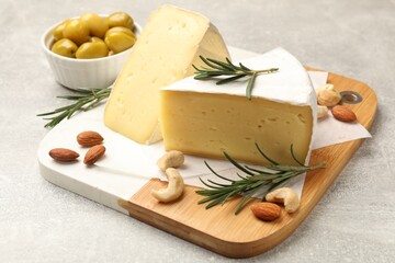 Pieces of tasty camembert cheese, rosemary, nuts and olives on grey textured table, closeup