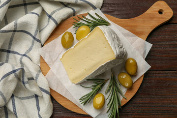 Board with piece of tasty camembert cheese, olives and rosemary on wooden table, top view