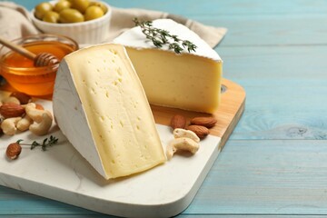 Tasty Camembert cheese with thyme, honey and nuts on light blue wooden table. Space for text
