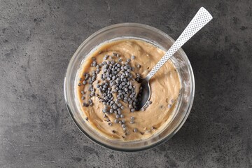 Raw dough with chocolate chips in bowl on grey table, top view