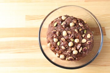 Raw chocolate dough with nuts in bowl on wooden table, top view. Space for text
