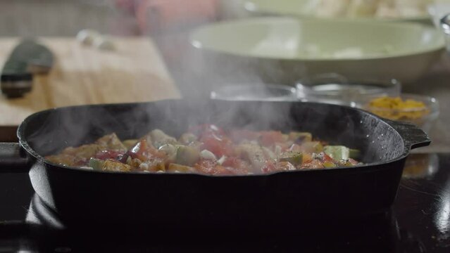 Close-up of steamed vegetables - tomatoes and zucchini - sprinkled with dried cumin by a skilled chef in a restaurant. Close up. Slow motion.