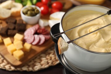 Fondue with tasty melted cheese, forks and piece of bread on table, closeup. Space for text