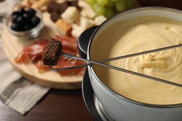 Fondue with tasty melted cheese, forks and piece of bread on wooden table, closeup
