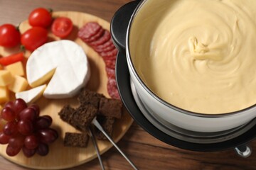 Fondue with tasty melted cheese, forks and different snacks on wooden table, above view