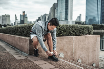 A man tying shoelaces on sport shoes in the city center park before cardio workout, running. ...