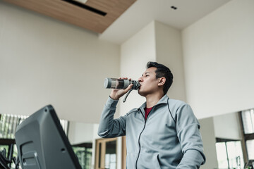 A man drinking water on treadmill in gym. Fitness, gym, workout and lifestyle concept.