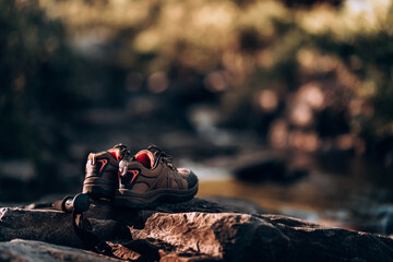 Hiking shoes and trekking pole on the rocks by the stream from the waterfall. - obrazy, fototapety, plakaty