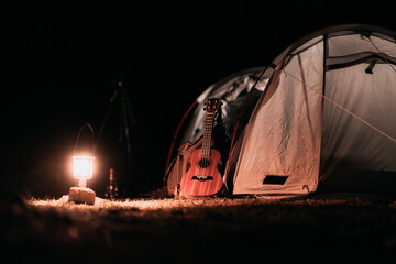 Ukulele on the ground in front of tents pitched on hillsides beside streams of water from waterfalls at night under star in the sky.