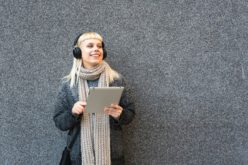 Portrait of young confident fashionable freelance woman with cool attitude working on digital tablet outside office building. Hipster stylish female posing against black wall.
