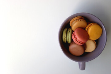 Purple cup filled with pastel macarons on white background. Top view.