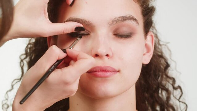 Eye shadow makeup to the upper eyelid, close-up. Makeup artist applies a bright eye shadow with a make-up brush.Tutorial master class of professional makeup, smoky eyes 