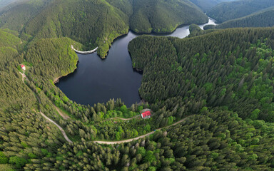 Aerial drone view above Gatu Berbecului lake at sunset. The water is hold by an arched concrete...