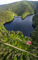 Vertical aerial drone view above Gatu Berbecului lake at sunset. The water is hold by an arched concrete dam, built within the wilderness of Cindrel Massif. Carpathia, Romania. - obrazy, fototapety, plakaty