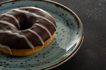 Donut with chocolate on a blue plate on a black table. Close-up.