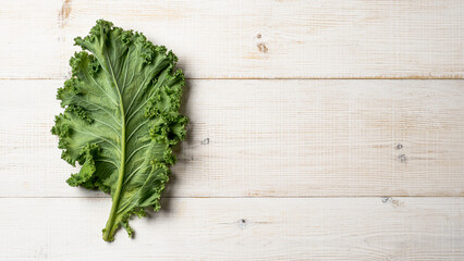 Green kale leaf on white wood table, copy space, top view
