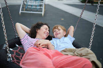 Obraz premium Happy Young mother playing with her son on the playground, hugging, laughing. having fun together on the weekend sunny day. School playground. High quality photo