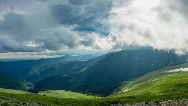 Sun shining through stormy clouds above Parang mountains. A dramatic sky can be seen as sun rays are penetrating the rainy clouds. Carpathian Massif, Romania.
