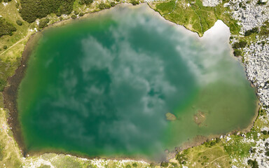 Clouds mirroring in an alpine lake waters. The clear waters of the glacier lagoon are blue and are reflecting the clouds and the sky. Drone view. Carpathia, Romania.