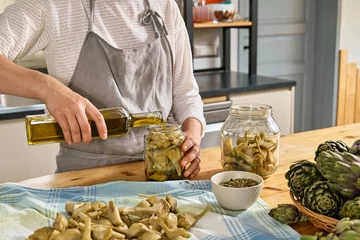 Foto op Canvas Woman preparing canned italian artichokes in olive oil. Artichoke hearts pickled with olive oil and herbs. Homemade healthy eating. © Caterina Trimarchi