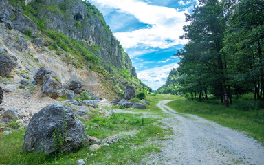 A dirt road winding along a rocky hill side. Large boulders have fallen from the side cliffs, and...