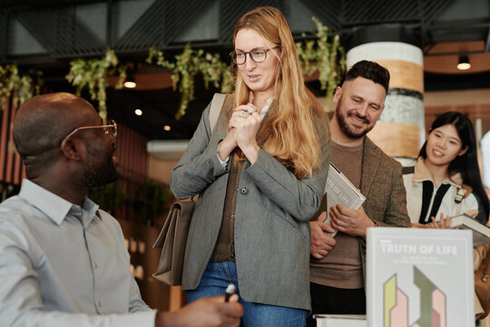 Young fan of famous writer talking to him during autograph session against other people standing in queue