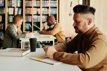 Side view of mature man in casualwear texting in smartphone or scrolling through online information in reading hall
