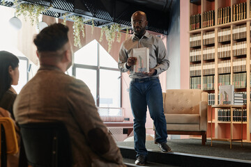 Confident male writer coming down stage with armchair and looking at public during presentation of his new book