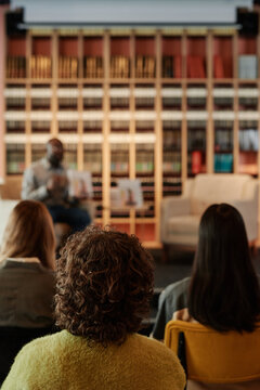 rear view of several female readers sitting in rows in front of stage with their favorite author presenting them his new book