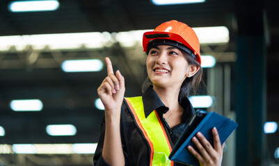 A woman wearing a safety vest and a hard hat is pointing to something on a tablet. She is smiling...