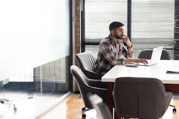 Asian male, looking thoughtful at laptop in modern business office