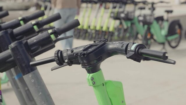 A high-resolution image featuring the close-up details of electric scooter handlebars with a blurred background of an urban scooter park, showcasing modern city transport.