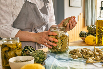 Woman preparing canned italian artichokes in olive oil. Artichoke hearts pickled with olive oil and...