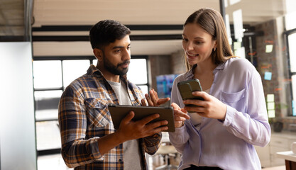 Asian male and Caucasian female colleagues are looking at tablet and smartphone in a modern business