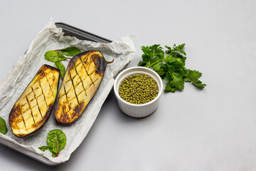 Baked eggplant halves in pallet.  Parsley leaves and mung bean in bowl - obrazy, fototapety, plakaty