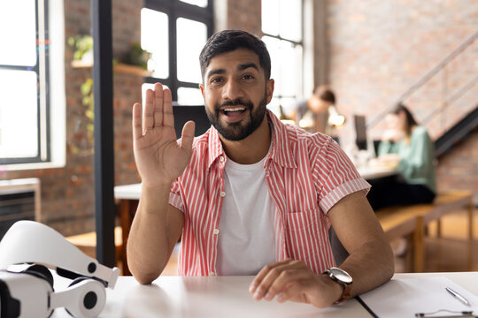 A young Asian male professional wearing striped shirt is waving on video call