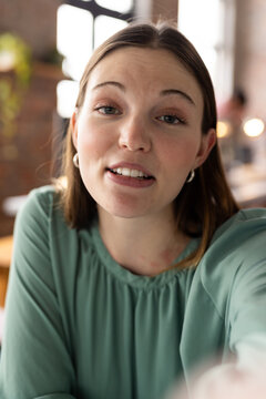 Caucasian female young professional looking at camera on video call, wearing green top