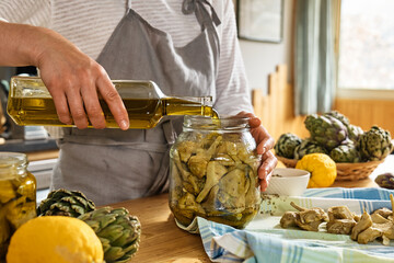 Woman preparing canned italian artichokes in olive oil. Artichoke hearts pickled with olive oil and...