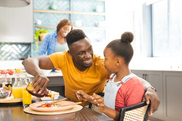 African American father serving breakfast to his daughter at home, mother in background