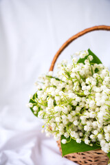 Basket with lilies of the valley on a white background. Vertical photo. Copy space. Selective focus.