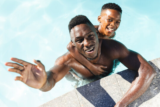 African American father and son enjoying swimming in pool at home