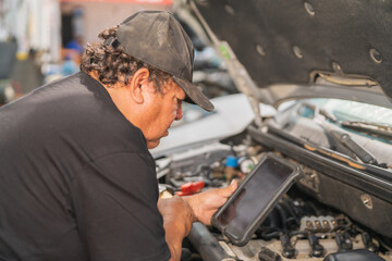 Mature mechanic using electronic device to inspect a car
