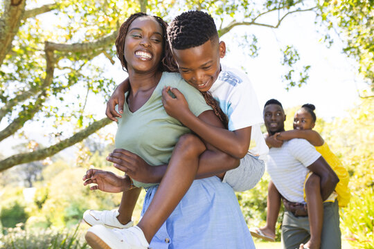 African American mother carrying young son, father watching, enjoying outdoors
