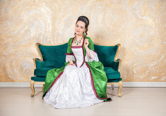 Beautiful smiling woman in green rococo style medieval dress sitting on the sofa