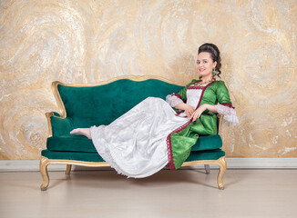 Beautiful smiling woman in green rococo style medieval dress lying down on the sofa